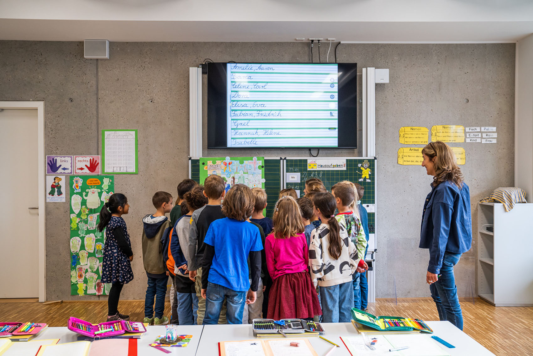 19 Schüler stehen interressiert vor der Tafel über der ein großes Videoboard hängt