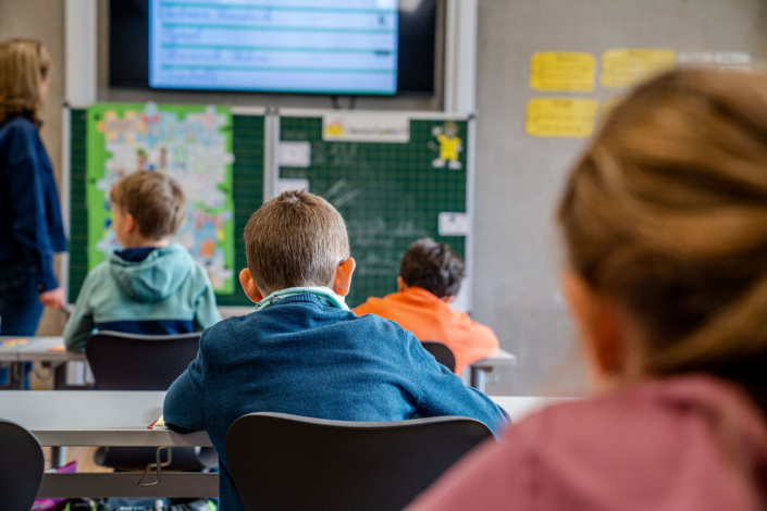 4 Schüler und die Lehrerin von hinten mit Blick auf die Tafel und Videowand